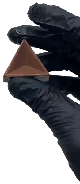 A hand in a black food-safe glove holding a milk chocolate pyramid chocolate